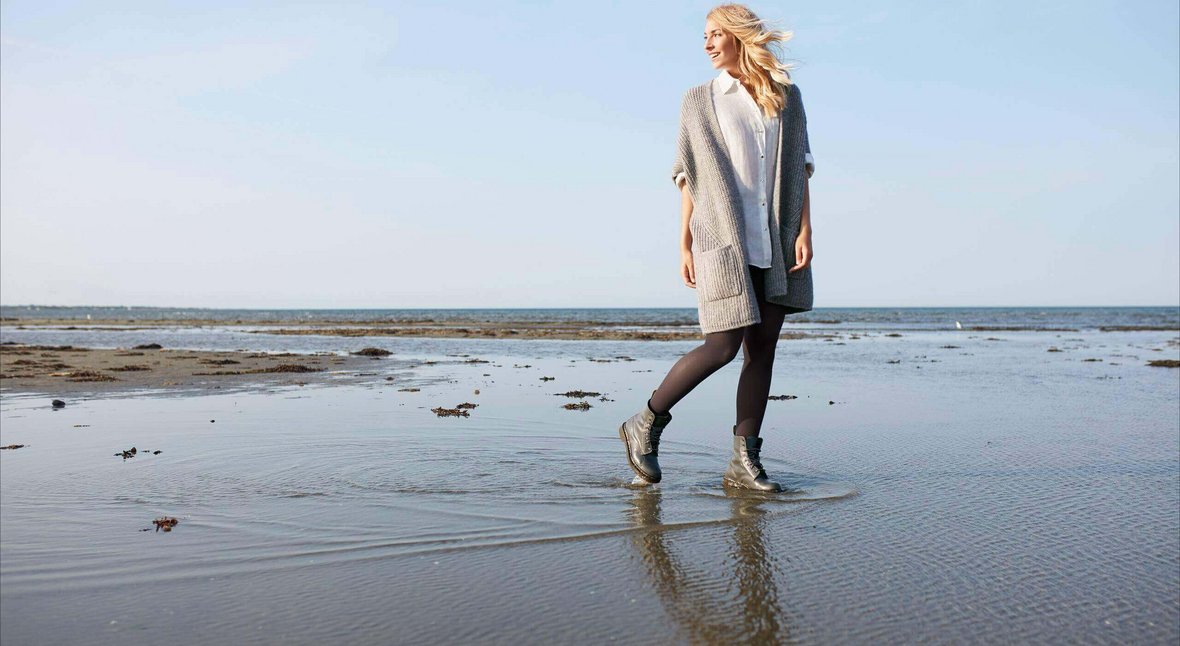 Eine junge Frau läuft an einem Meeresstrand entlang. Sie trägt schwarze Kompressionsstrümpfe von Bauerfeind. Diese fördern die Durchblutung und wirken der Entstehung von Krampfadern sowie Besenreisern entgegen.